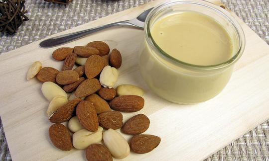 Light, home-made almond puree in glass jar, with almonds next to it. Light, home-made almond puree in glass jar, with almonds next to it.