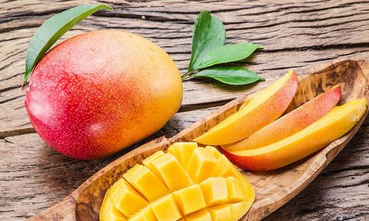 Mango, roh - Mangifera indica: Mango in Häppchen geschnitten in Holzgefäss vor einer ganzen Mango.