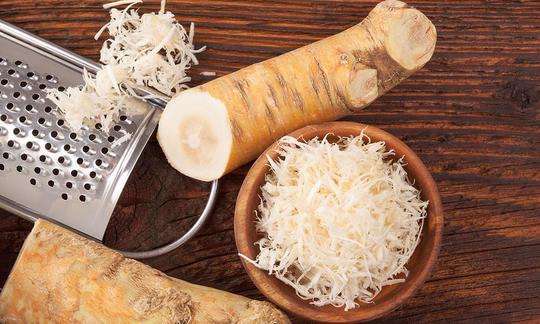 Meerrettich - Armoracia lapathifolia: Als Wurzel und gerieben, links das einfache Reiberzeugnis auf einem dunklen Holztisch. Horseradish—Armoracia lapathifolia: Both the root and grated, on the left is freshly grated root.