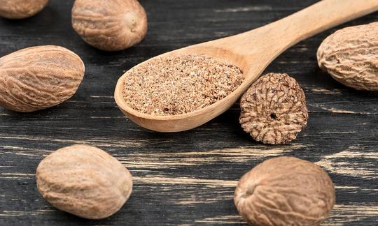 Мускатный орех - Myristica fragrans: деревянная ложка с тертым мускатным орехом, рядом цельные орехи