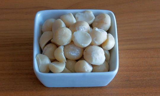 Macadamian nuts in a bowl. As a result of cultivation, processing, and demand, macadamian nuts are among the most expensive nuts in the world. Macadamia nuts, cracked, raw in porcelain dish white on table.