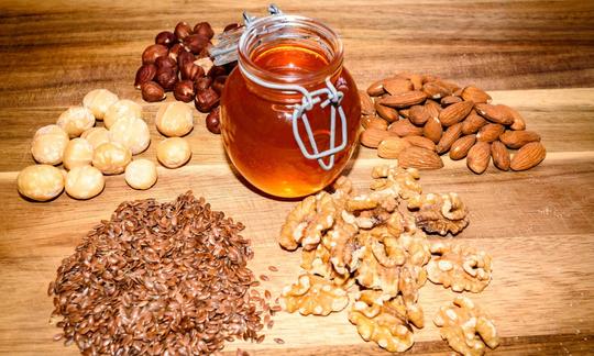 Zutaten für den "Natura Sanat Honig-Mix mit Macadamia", ausgelegt auf einem Holztisch.