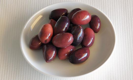 Aceitunas en un bol: las aceitunas son frutos con hueso de los olivos, que el hombre lleva cultivando desde el S.IV a.C. para distintos usos. Olive scure in una ciotola bianca: le olive sono drupe di olive.