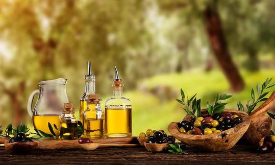 Im Vordergrund links Olivenöl in Glasgefässen, rechts daneben Oliven in Holzbehälter.
