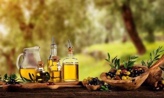 Aceite: en primer plano a la izquierda, aceite de oliva en recipientes de metal; a su lado, un recipiente de madera con olivas y un olivar de fondo. Aceite: Primer plano a la izquierda Aceite de oliva en frascos de vidrio.