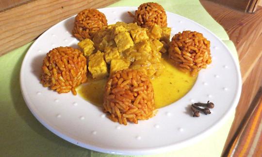 Il "Tempeh con curry all'arancia e riso speziato" è finito e servito su un piatto.