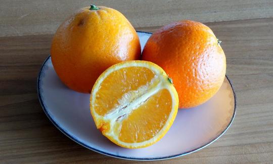 Drei Orangen auf einem weissen Teller, die Orange im Vordergrund ist halbiert. Drei Orangen auf einem weissen Teller, die Orange im Vordergrund ist halbiert.