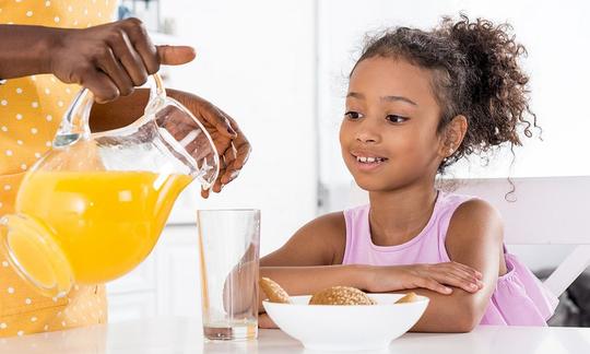 Afroamerikanische Mutter giesst frisch gepressten Orangensaft in das Trinkglas Ihrer Tochter.