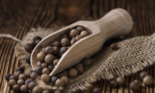 Allspice, whole grains in a wooden scoop and around it on sackcloth. Allspice, whole grains in a wooden scoop and around it on sackcloth.