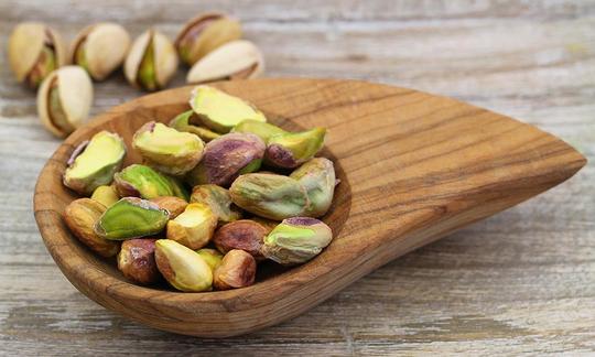Pistachios, opened, raw - Pistacia vera in miniature wooden bowl, behind 6 with shell.