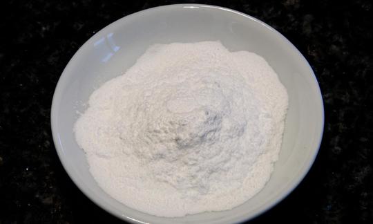 Azúcar glas en un bol: el azúcar glas es un alimento crudo que se consigue moliendo azúcar blanco refinado. Zucchero a velo in una ciotola: un prodotto grezzo ottenuto dalla macinazione dello zucchero bianco.