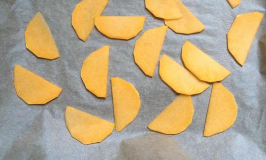 Lasaña con crema de anacardos y pesto de col rizada: rodajas de calabaza moscata con aceite, sal y pimienta en una bandeja de horno con papel vegetal.