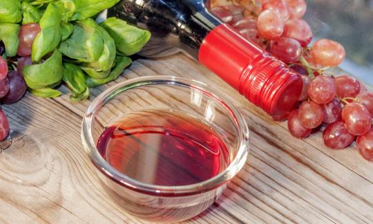 Vinagre de vino tinto en un recipiente de vidrio rodeado de uvas y albahaca. Vinagre de vino tinto en un recipiente de vidrio rodeado de uvas y albahaca.