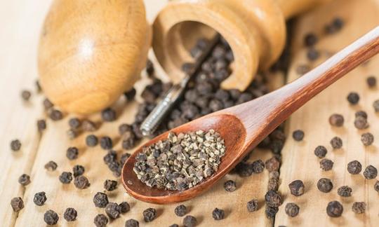 Black pepper (Piper nigrum), black peppercorns on a table and spoon with crushed pepper.