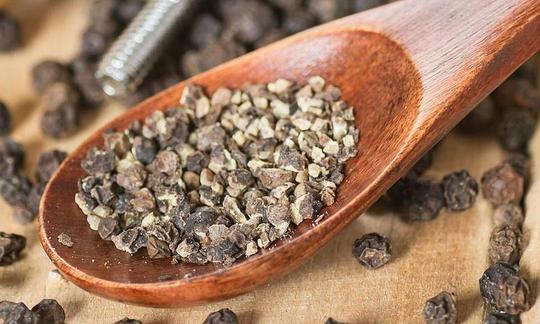 Деревянная ложка с молотым на мельнице чёрным перцем. Рядом целые горошины черного перца. Деревянная ложка с молотым на мельнице чёрным перцем. Рядом целые горошины черного перца.