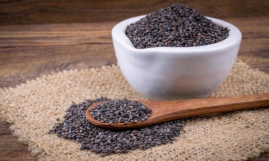 Black sesame seeds (Sesamum indicum) in a bowl, on a wooden spoon, and  sprinkled out under spoon.
