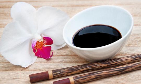Sweet soy sauce in a small white porcelain bowl, surrounded by two chop sticks and blossom.