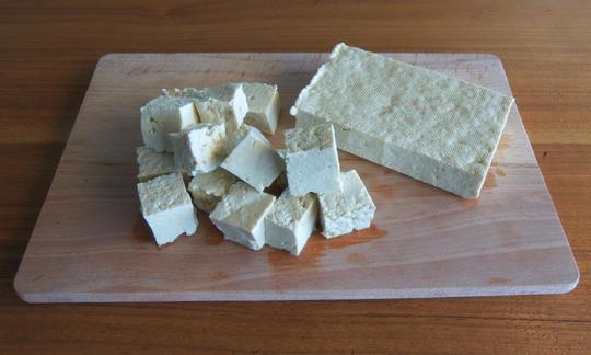 Geschmacksneutraler Tofu als ganzer Block und in Stücken auf einem Schneidbrett.