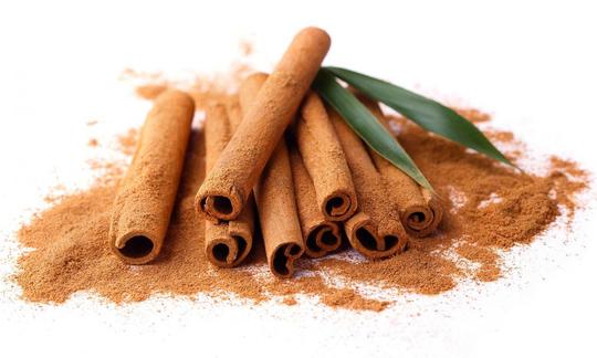 Ground cinnamon—Cinnamomum aromaticum—with cinnamon sticks and two unrelated leaves on top.