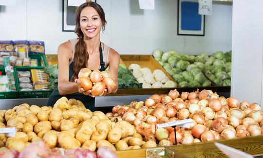 Onion raw, untreated - Allium cepa: young female seller shows us a handful of yellow onions. Onion raw, untreated - Allium cepa: young female seller shows us a handful of yellow onions.