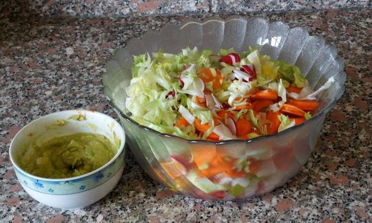 Готовый салат из сырых овощей рядом с миской, наполненной дрессингом из авокадо и лимона.