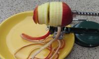 Apple peeler, apple and plate: apple being peeled, half-peeled raw apple