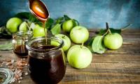 Homemade apple syrup (apple butter) in mason jar with apples behind it.