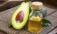 Avocado oil (Persea americana): an avocado cut in half with a bottle of  avocado oil next to it.