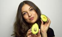 A woman displays the two halves of an avocado which has been cut open.