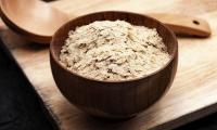 Brewer's yeast (Saccharomyces cerevisiae) in flakes in wooden bowl, next to wooden spoon on board.