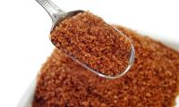 A spoon of coarse brown sugar held over a jar of brown sugar.