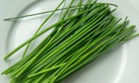 Raw, untreated chives (Allium schoenoprasum) on a white plate.