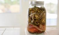 Jalapeños in a jar with screw cap - on white tales.