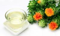 Bowl of safflower oil on the left and the fresh flowers on the right.