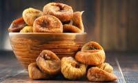 Dried figs in round wooden vessel plus five next to it.