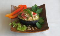 Meal "Avocado with tomato and banana filling and pine nuts", served on a square wooden plate.