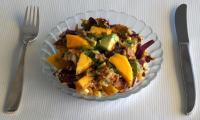 Готовый «Салат Батавия с овощами и манго с заправкой из орехов и чиа» на стеклянной тарелке.
