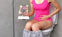 Mujer joven con intestino irritable en el inodoro, que muestra un modelo del colon.