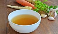 Vegan vegetable broth — extra low in salt — in a white ceramic bowl,  ingredients in the background.