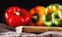 Сладкий перец, Capsicum annuum, сырые: красный, желтый и зеленый на деревянной тарелке.