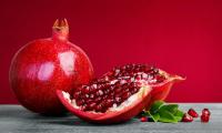 Pomegranate (Grenadine, Punica granatum) broken up next to it and seeds in front of red background.