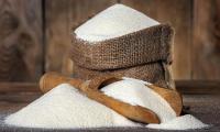 Semolina raw on wooden table with wooden ladle and sack standing behind.