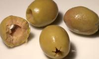 Pitted olives spread out on a white background. The olives on the left side are halved.