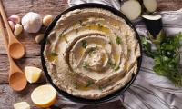 Eggplant hummus with sesame, onions and garlic in black bowl.