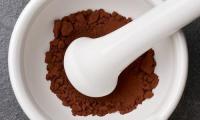 Cocoa powder, raw and unsweetened, in a white ceramic mortar and pestle.