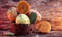 Fresh prickly pears in a rusted tin container, one of which is cut open (Opuntia spp).