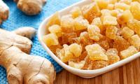 Ginger, candied (ginger root) in a white bowl, to the left of it ginger roots, the rhizome.