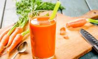 A glass of carrot juice, freshly squeezed, with carrots on a wooden cutting board