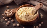 Chickpea flour in wooden bowl surrounded by chickpeas. - Cicer arietinum.