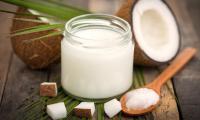 Glass container and wooden spoon with coconut oil — pieces of coconut in  the foreground.